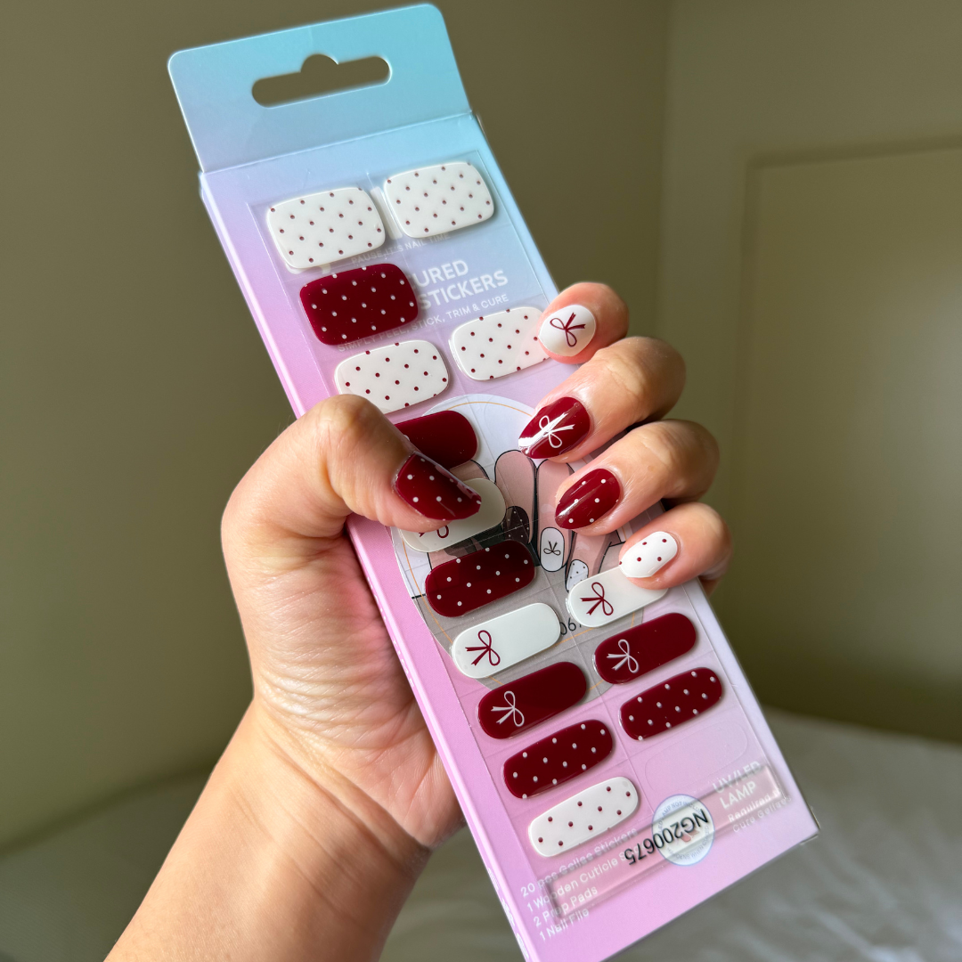 Hand holding a package of gellae red and white nail stickers with matching designs on nails.