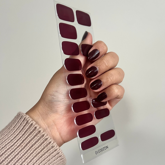 Hand holding a sheet of dark red nail stickers against a plain background