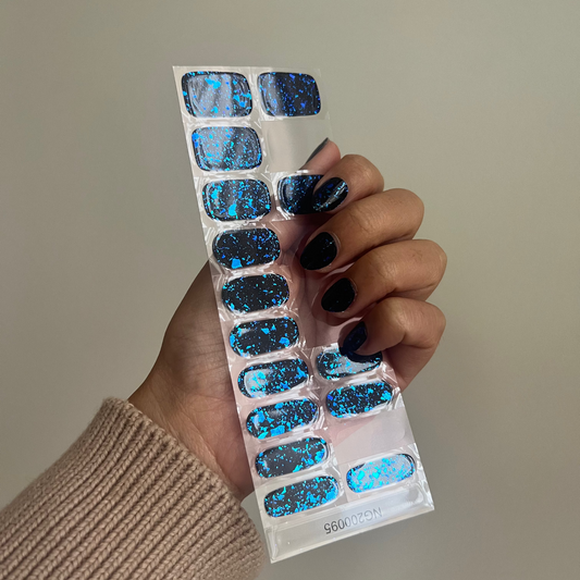 Hand holding a sheet of blue glittery nail art stickers against a neutral background